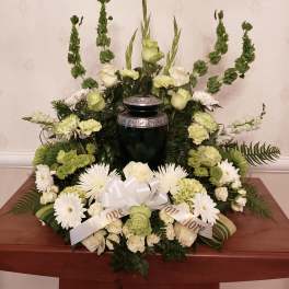 White and green funeral floral arrangement with a ribbon on a dark urn