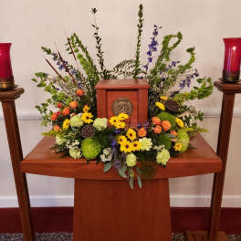 Symmetrical funeral floral arrangement around a wooden urn with red candles