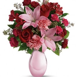 Pink lilies and red roses arranged in a pink glass vase