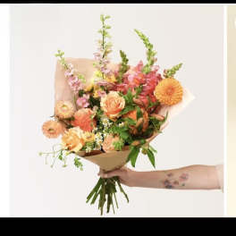 Handheld bouquet of peach roses, dahlias, and mixed flowers wrapped in brown paper