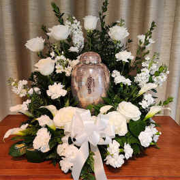 White floral funeral arrangement with a decorative urn and ribbon