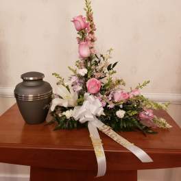 Pink and white funeral spray with urn and ribbon on a table