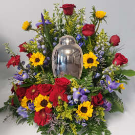 Colorful funeral spray with roses, sunflowers, and gerbera daisies around a silver urn