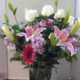 Bouquet of pink lilies, white roses, and purple flowers in a glass vase