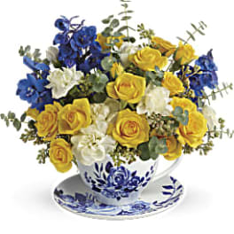 Yellow and blue roses arranged in a blue-and-white teacup and saucer