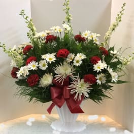 Red and white flower arrangement in a white pedestal vase with a red ribbon