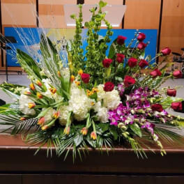 Large altar-style arrangement with red roses, white hydrangeas, orchids, tulips, and tall green spikes.