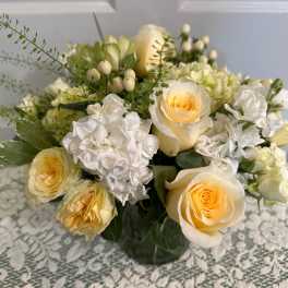 Low glass vase of pale yellow roses and white stock in a rounded arrangement