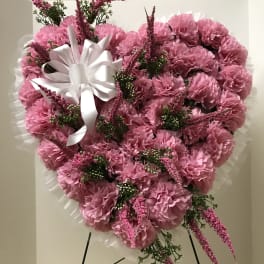 Heart-shaped pink carnation arrangement with a white ribbon bow