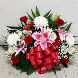 Red and white floral arrangement with pink lilies and a large red ribbon