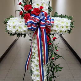 Large floral cross with white chrysanthemums, red carnations, and a red-white-blue ribbon