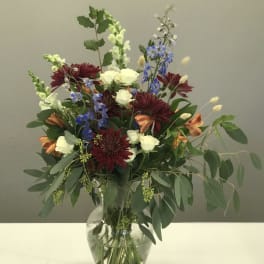 Mixed bouquet of burgundy, white, and blue flowers in a glass vase