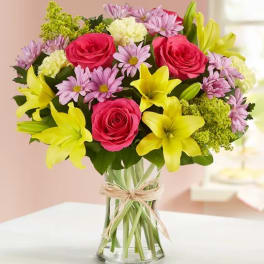 Bouquet of pink roses, yellow lilies, and lavender daisies in a glass vase