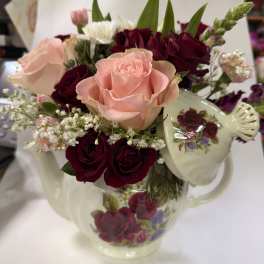 Pink and burgundy roses arranged in a floral teapot