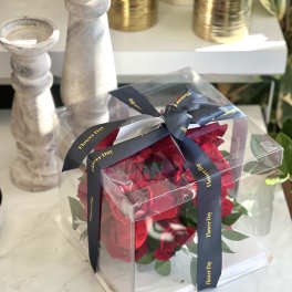 Red roses in a clear gift box tied with a dark ribbon