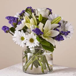 White lilies and daisies with purple filler in a glass vase