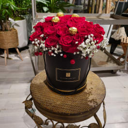 Red roses arranged in a black hatbox with gold-wrapped chocolates