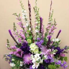 Tall purple and white floral arrangement in a dark vase