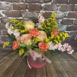 Pink and peach roses with yellow filler flowers in a round vase