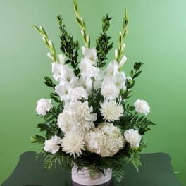 White floral arrangement in a white basket with tall gladiolus and hydrangeas