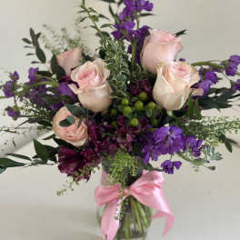Vase of light pink roses with purple stock and alstroemeria, tied with a pink ribbon.