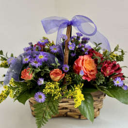 Basket of orange roses and purple daisies with a lavender ribbon