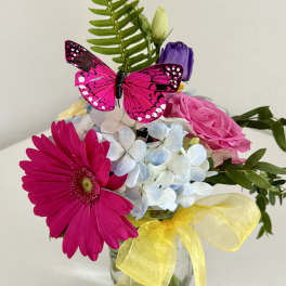 Bouquet of pink and white flowers in a glass vase with a yellow ribbon and butterfly decoration