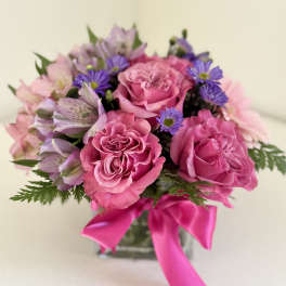 Pink roses and purple flowers in a glass vase with a bright pink ribbon
