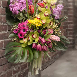 Tall tropical bouquet in a clear vase with orchids, lilies, and pink blooms