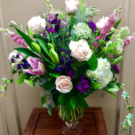 Mixed bouquet of pale pink roses, lilies, and purple flowers in a glass vase