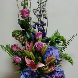 Tall bouquet of pink lilies, roses, and blue hydrangeas in a glass vase