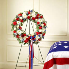 Red, white, and blue floral wreath on a stand with ribbon streamers