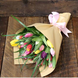 Bouquet of multicolored tulips wrapped in tan paper with a pink ribbon