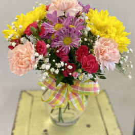 Colorful bouquet of carnations and daisies in a glass vase with a plaid ribbon