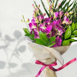 Bouquet of purple orchids wrapped in cream paper with a pink ribbon