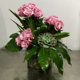 Pink roses arranged in a glass vase with broad green leaves