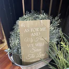 Decorative greenery arrangement in a metal basket with a scripture sign