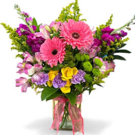 Mixed bouquet of pink gerbera daisies, purple flowers, and yellow roses in a glass vase