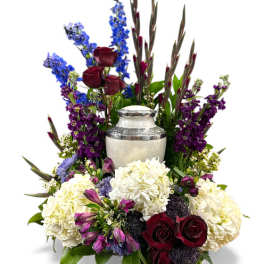 Funeral urn surrounded by white hydrangeas, red roses, and purple flowers