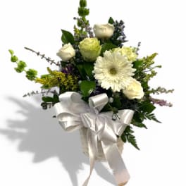 White and pale yellow flowers in a white basket with a satin bow