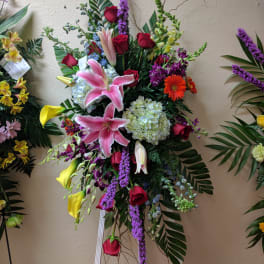 Tall standing floral spray with pink lilies, red roses, and purple accents