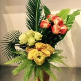 Bouquet of yellow, red, and white flowers in a vase with tropical leaves