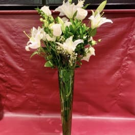 White lilies and roses arranged in a tall glass vase