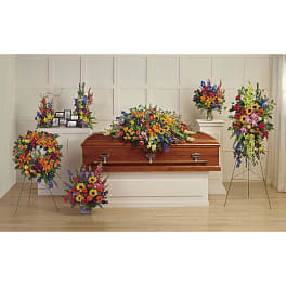 Colorful funeral casket spray with standing floral tributes around a wooden casket