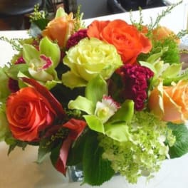 Mixed bouquet of orange and green roses with orchids in a glass vase