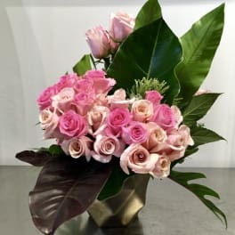 Pink roses arranged in a gold vase with large tropical leaves