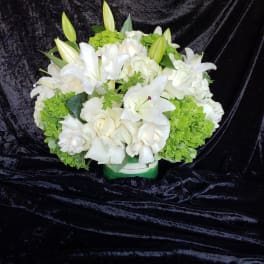 White lilies and roses arranged with green hydrangeas in a low container