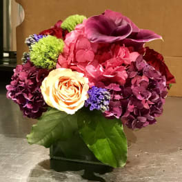 Colorful floral arrangement in a square vase with pink, purple, and yellow blooms