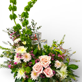 Pink roses and white daisies arranged around a clear glass cross