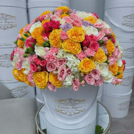 Round bouquet of pink, yellow, white, and lavender roses in a white hat box